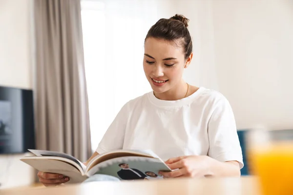 Foto Alegre Hermosa Mujer Leyendo Revista Sonriendo Mientras Está Sentado — Foto de Stock