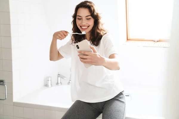 Banyoda Cep Telefonu Kullanırken Gülümseyen Diş Temizleyen Güzel Bir Kadının — Stok fotoğraf
