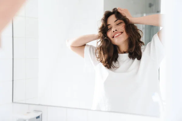 Foto Mulher Branca Sorridente Agarrando Cabeça Enquanto Olha Para Espelho — Fotografia de Stock