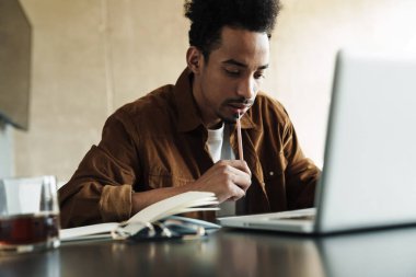 Afro-Amerikan bir adamın oturma odasında çalışırken dizüstü bilgisayar kullanması düşüncesi.