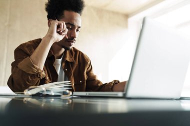 Afro-Amerikan bir adamın oturma odasında çalışırken dizüstü bilgisayar kullanması düşüncesi.