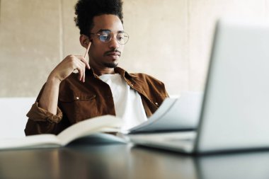 Gözlüklü Afro-Amerikan bir adamın oturma odasında çalışırken dizüstü bilgisayar kullanması.