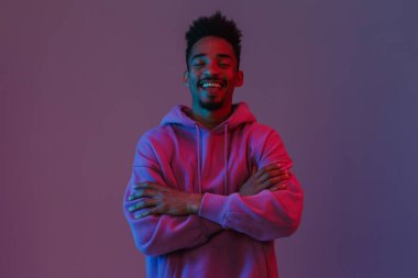 Siyahi kapüşonlu gülümseyen Afrikalı Amerikalı adamın portresi. Kameraya zehirlenmiş, kollarını bağlamış, menekşe arka planında izole bir şekilde.