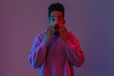 Şok olmuş renkli kapüşonlu Amerikalı bir adamın portresi zehirleniyor ve mor arka planda izole edilmiş kameraya bakıyor.