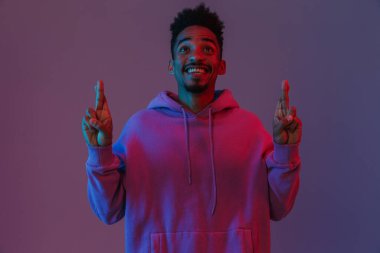 Renkli kapüşonlu Amerikalı iyimser adamın portresi. Kameraya zehirlenmiş, parmaklarını menekşe arka planında çapraz yapmış.