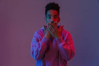 Siyahi kapüşonlu Afro-Amerikan bir adamın portresi. Kameraya zehirleniyor. Elleri ağzında, menekşe arka planında.