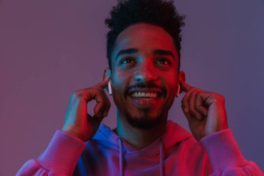 Siyahi kapüşonlu gülümseyen Afrikalı Amerikalı adamın portresi. Mor arka planda izole edilmiş kulaklıklarla müzik dinliyor.
