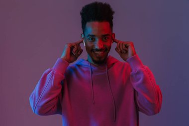 Renkli kapüşonlu Afro-Amerikan adamın portresi. Mor arka planda izole edilmiş kulaklıkları olan müzik dinliyor.