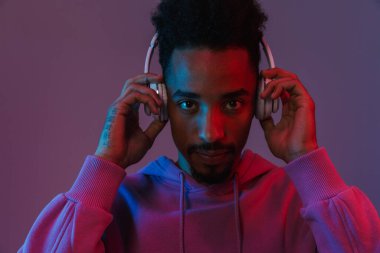 Renkli kapüşonlu Amerikalı sıradan bir adamın portresi. Mor arka planda izole edilmiş kulaklıklarla müzik dinliyor.