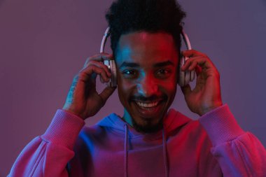 Siyahi kapüşonlu gülen Amerikalı adamın portresi. Menekşe arka planda izole edilmiş kulaklıklarla müzik dinliyor.