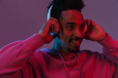 Renkli kapüşonlu Afro-Amerikan bir adamın portresi. Mor arka planda izole edilmiş kulaklıklarla müzik dinliyor.