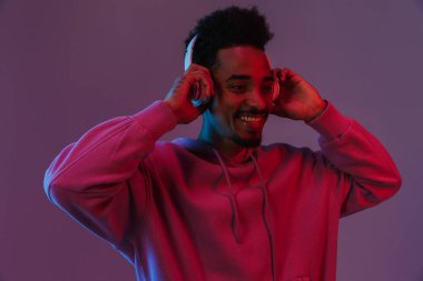 Esmer Afro-Amerikan kapüşonlu adam portresi. Mor arka planda izole edilmiş kulaklıklarla müzik dinliyor.