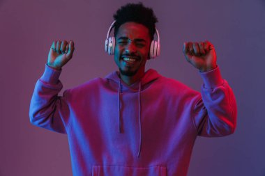 Heyecanlı, renkli kapüşonlu Amerikalı bir adamın portresi. Menekşe arka planda izole edilmiş kulaklıklarla müzik dinliyor.