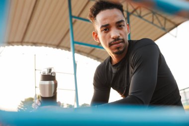 Spor stadyumunda otururken elinde su şişesi tutan Afro-Amerikan bir adamın görüntüsü