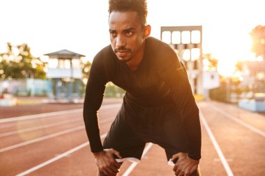 Konsantre olmuş Afro-Amerikan bir adamın spor sahasında koşması.