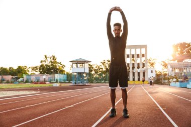 Spor stadyumunda vücudunu esneten Afro-Amerikan bir adamın resmi.