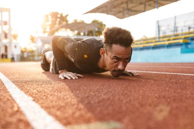 Açık havada antrenman yaparken spor stadyumunda uzanan güçlü bir Afrikalı Amerikalı.