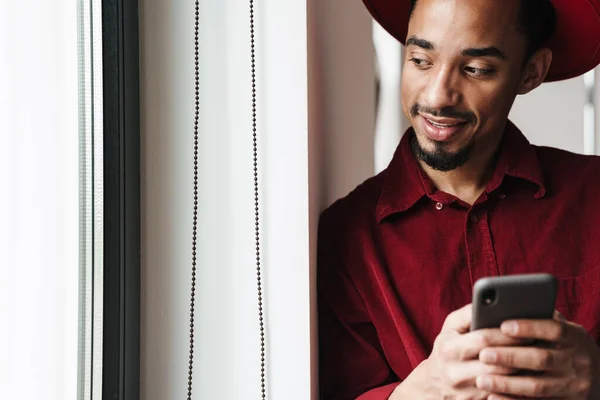 Schöner Lächelnder Stylischer Junger Afrikanischer Mann Mit Handy Während Drinnen — Stockfoto