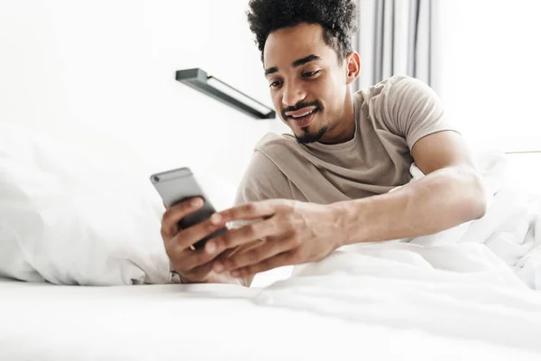 Foto Hombre Afroamericano Sonriente Con Bigote Usando Teléfono Móvil Cama —  Fotos de Stock