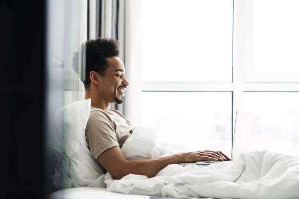 Photo Laughing African American Man Working Laptop While Lying Bed — Stock Photo, Image