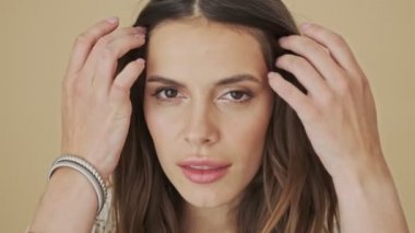 Çekici genç bir kadının yakın çekim görüntüsü stüdyodaki bej bir arka planda tek başına kameraya poz veriyor.