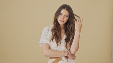 Muhteşem genç bir kadın kameraya poz veriyor. Stüdyoda bej bir arka planın başında duruyor.