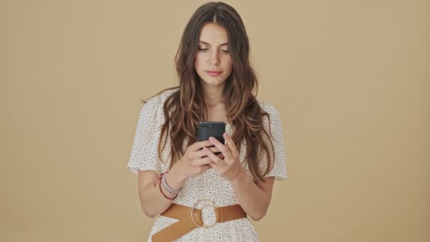 Piękna Młoda Kobieta Używa Swojego Smartfona Stojącego Nad Beżowym Tłem — Wideo stockowe