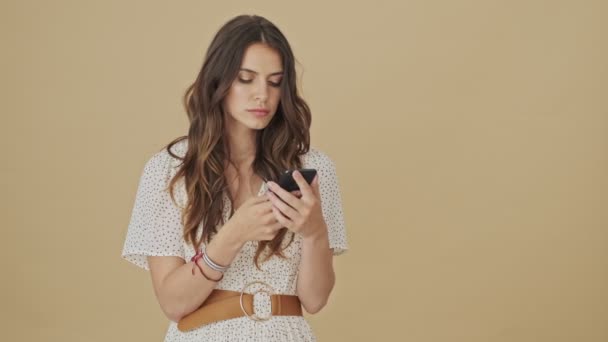 一位专心致志的年轻女子正站在工作室的米色背景旁 在智能手机上打字 — 图库视频影像
