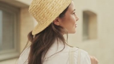 Şapka takan, kahve içen ve sokakta yürürken etrafa bakınan çekici bir kadın.