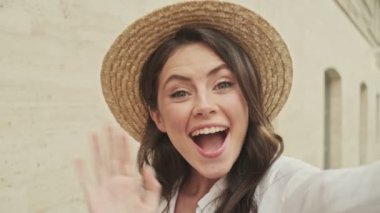 Dışarıda duvarın yanında dikilirken videoyla konuşan neşeli, çekici bir kadın.