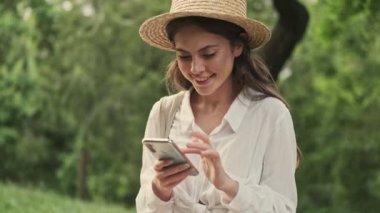 Parkta otururken akıllı telefon kullanan mutlu ve çekici bir kadın.