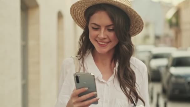 Sorrindo Mulher Atraente Usando Chapéu Usando Smartphone Enquanto Caminha Rua — Vídeo de Stock