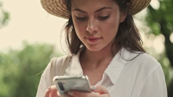 Sorrindo Mulher Atraente Usando Chapéu Escrevendo Mensagem Smartphone Enquanto Sentado — Vídeo de Stock