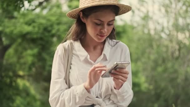 Усміхнена Приваблива Жінка Капелюсі Дивиться Камеру Стає Щасливою Використовуючи Смартфон — стокове відео