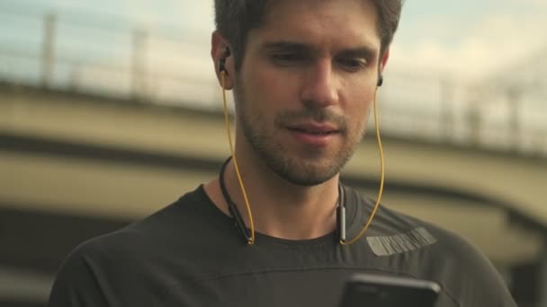 Homem Concentrado Com Fones Ouvido Está Usando Smartphone Enquanto Caminha — Vídeo de Stock