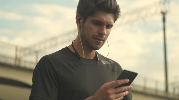 一个严肃的男人正在使用他的健身跟踪器 并在靠近桥边的城市里用他的智能手机连接它 — 图库视频影像
