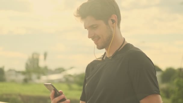 Een Aantrekkelijke Sporter Met Oortjes Gebruikt Zijn Smartphone Tijdens Het — Stockvideo