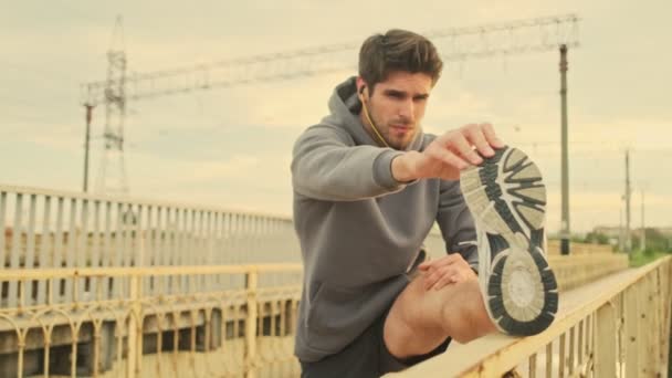 Kulaklıklı Genç Bir Sporcu Köprüde Egzersiz Yaparken Bacaklarını Esnetiyor — Stok video