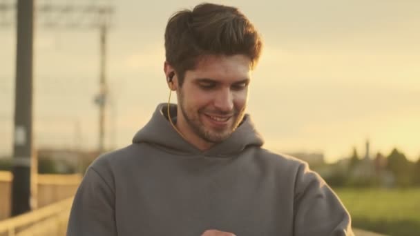 Jovem Desportista Sorridente Com Fones Ouvido Está Andando Ponte Pela — Vídeo de Stock