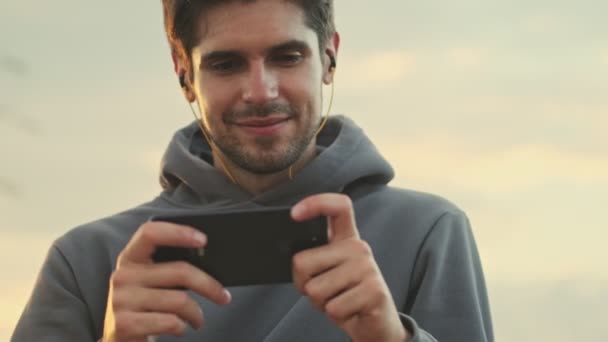 Jovem Esportista Positivo Está Assistindo Algo Seu Smartphone Segurando Horizontalmente — Vídeo de Stock