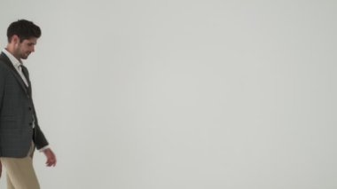 Genç, mutlu, sakallı iş adamı beyaz duvar arkasında tek başına yürüyor.