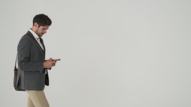 年轻快乐的 满脸胡须的生意人 独立行走在白墙的背景下 一边用手机 — 图库视频影像