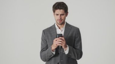 Genç ve ciddi bir iş adamı cep telefonu kullanırken beyaz duvar arkasında izole edilmiş.