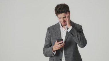 Genç üzgün, kafası karışık iş adamı cep telefonu kullanırken beyaz duvar arkaplanından izole edilmiş