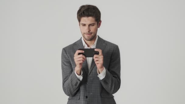 Yoğunlaşmış Adamı Cep Telefonuyla Oyun Oynarken Beyaz Duvar Arkaplanı Üzerinde — Stok video