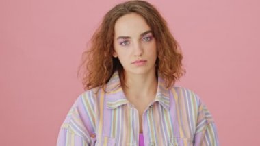 Ciddi bir genç kadın kameraya orta parmağını gösteriyor. Stüdyoda pembe bir arka planda tek başına duruyor.