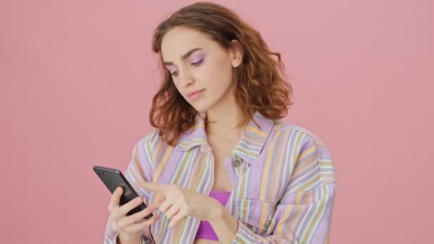 Задоволена Молода Жінка Друкує Своєму Мобільному Телефоні Стоячи Ізольовано Рожевому — стокове відео