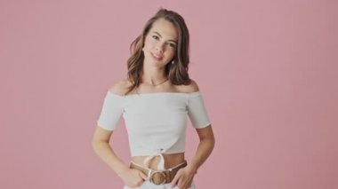 Güzel bir genç kadın birini dinliyor ve pembe arka plandan izole edilmiş baş parmağını sallayarak stüdyoda işaret veriyor.
