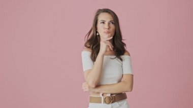 Çekici genç bir kadın stüdyoda pembe arka planda duran bir şey düşünüyor.