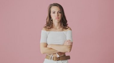 Üzgün genç bir kadın kollarını tutarken stüdyoda pembe arka planda izole bir şekilde duruyor.